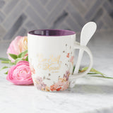Purple Floral Ceramic Coffee Mug with Spoon and Soft Pink Flowers in Background