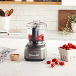 Food processor on marble countertop with red grape tomatoes in basket and also in food processor.